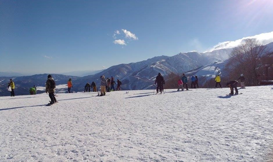 Skiers waiting at the top of a ski slope. A snowy mountain range is visible in the distance