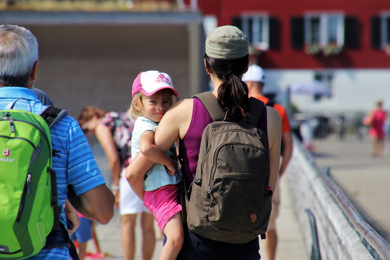 A woman wearing a backpack is holding a young girl