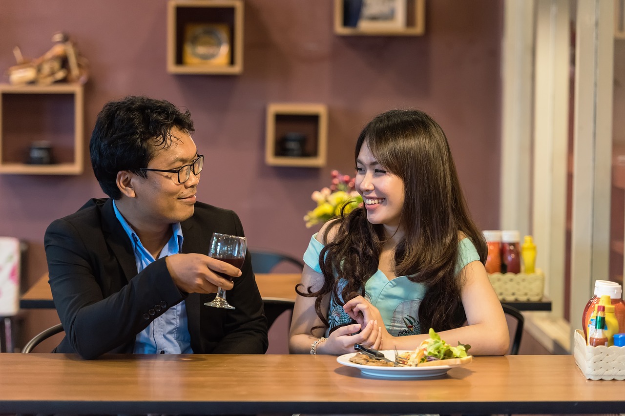 A Japanese couple sitting in a restaurant, talking. The man is holding a glass of wine.